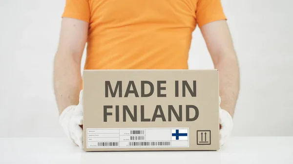 El hombre pone una caja de cartón con texto MADE IN FINLAND sobre la mesa —  Fotos de Stock