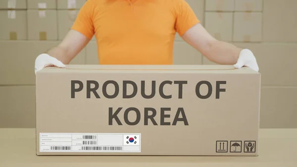 Magazijnmedewerker en grote doos met PRODUCT VAN KOREA gedrukte tekst — Stockfoto