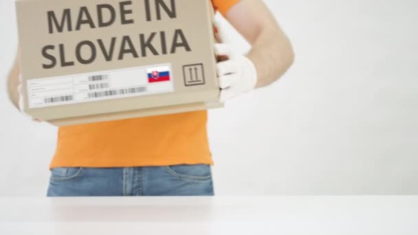 Pracovník v oranžové uniformě dává krabici s nápisem MADE IN SLOVAKIA na stůl — Stock video