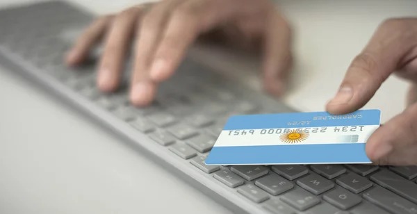 Homme inconnu paie en ligne avec une carte bancaire en plastique avec le drapeau imprimé de l'Argentine. Numéros fictifs — Photo