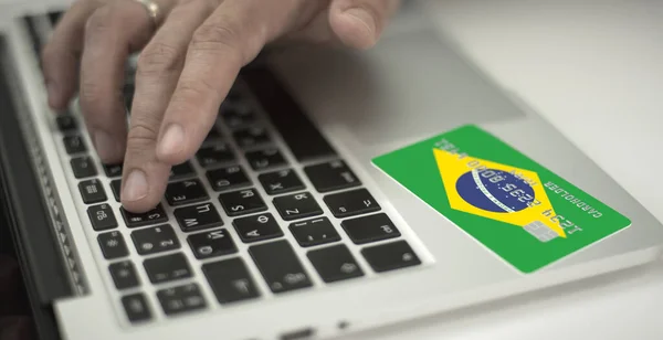 Man betaalt online met plastic bankkaart met afgedrukte vlag van Brazilië. Fictieve nummers — Stockfoto