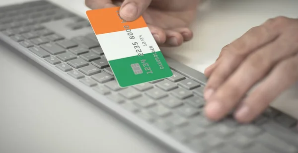 Homme paie en ligne avec une carte bancaire en plastique avec le drapeau imprimé de la République d'Irlande. Numéros fictifs — Photo
