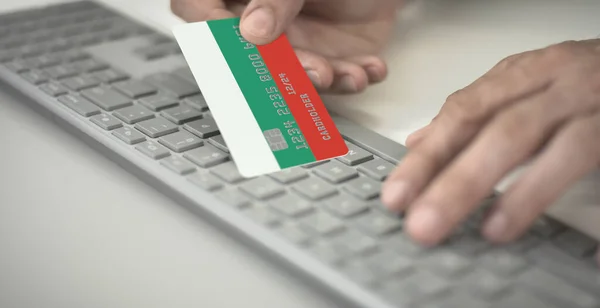Homme paie en ligne avec une carte bancaire en plastique avec le drapeau imprimé de la Bulgarie. Numéros fictifs — Photo