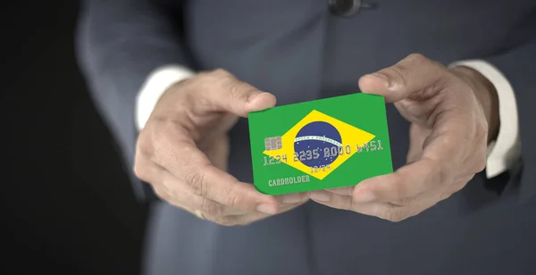 Empresário segurando cartão bancário de plástico com bandeira impressa do Brasil, números fictícios — Fotografia de Stock