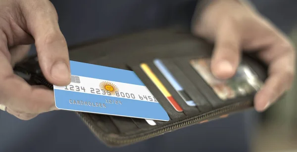 Бизнесмен вытаскивает кредитную карту с флагом Аргентины из бумажника, вымышленный номер карты — стоковое фото