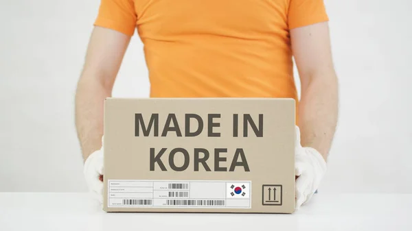 Работник в оранжевой униформе ставит коробку с печатью MADE IN KOREA на стол — стоковое фото