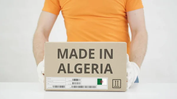 El hombre pone una caja de cartón con texto MADE IN ARGERIA sobre la mesa —  Fotos de Stock
