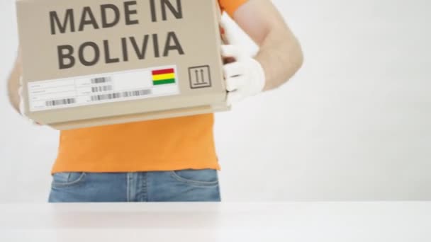 Man zet kartonnen doos met MADE IN BOLIVIA tekst op tafel — Stockvideo