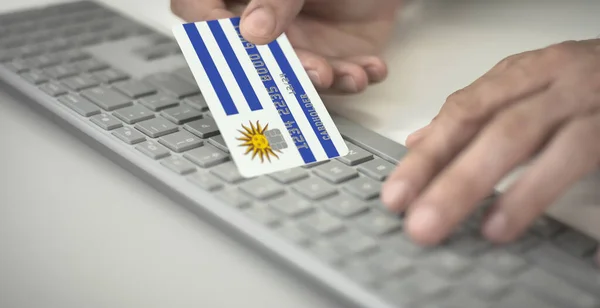 Man pays online with plastic bank card with printed flag of Uruguay. Fictional numbers — Stock Photo, Image