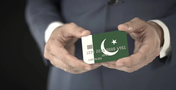 Businessman holds credit card with printed flag of Pakistan, fictional numbers — Stock Photo, Image