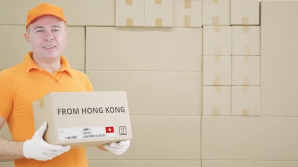 Warehouse worker holds cardboard box with printed FROM HONG KONG text on it — Stock Video