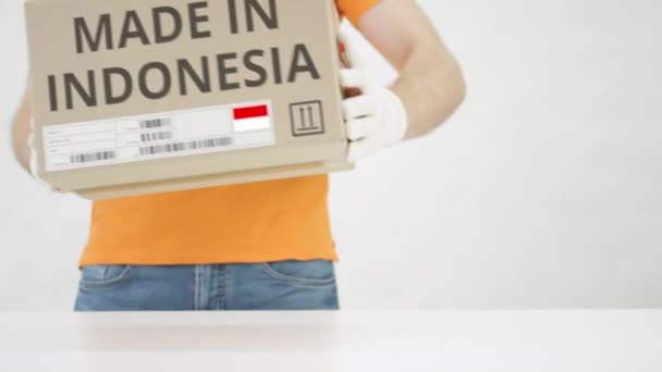 Un travailleur portant un uniforme orange met une boîte avec l'impression MADE IN INDONESIA sur la table — Video