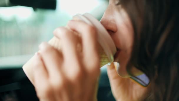 Mooie jonge vrouw drinkt koffie uit wegwerpbeker terwijl praten op de telefoon in een auto — Stockvideo