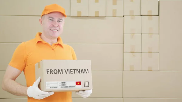 Trabajador vistiendo uniforme naranja sostiene caja con texto impreso de VIETNAM y etiqueta —  Fotos de Stock