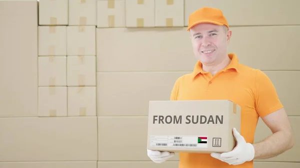 El trabajador del almacén sostiene la caja de cartón con el texto impreso de SUDAN en ella —  Fotos de Stock
