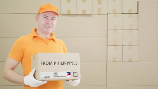 Pekerja gudang memegang kotak kardus dengan teks PHILIPPINES FROM yang dicetak di atasnya — Stok Foto