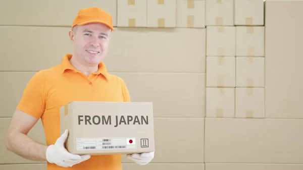 Trabajador vistiendo uniforme naranja sostiene caja con texto impreso de JAPÓN y etiqueta — Foto de Stock