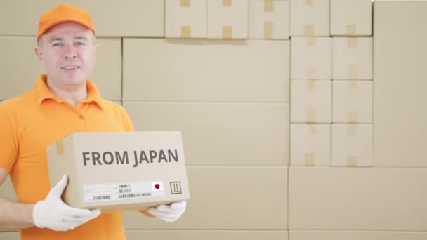 Trabalhador vestindo uniforme laranja mantém caixa com texto impresso do JAPÃO e etiqueta — Vídeo de Stock