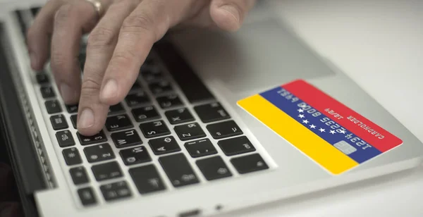 Homme paie en ligne avec une carte bancaire en plastique avec le drapeau imprimé du Venezuela. Numéros fictifs — Photo