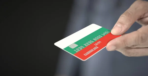 Man gives plastic bank card with printed flag of Bulgaria. Fictional numbers — Stock Photo, Image