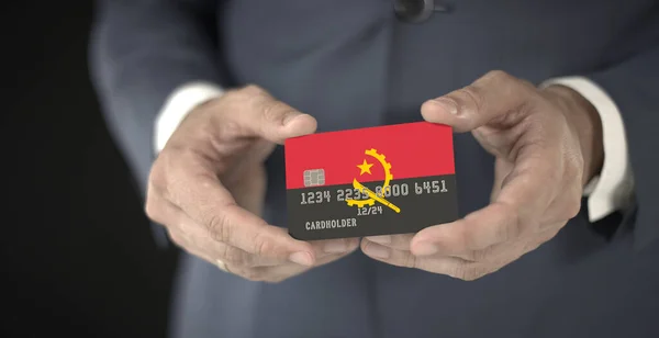 Businessman holding plastic bank card with printed flag of Angola, fictional numbers — Stock Photo, Image