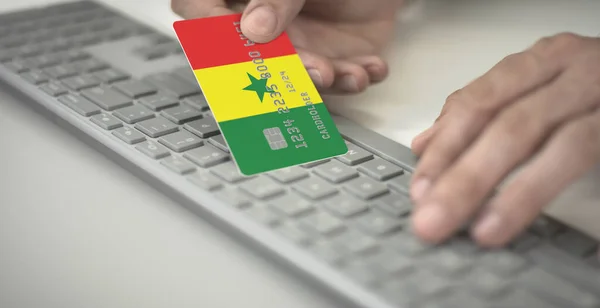 Homme paie en ligne avec une carte bancaire en plastique avec le drapeau imprimé du Sénégal. Numéros fictifs — Photo