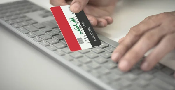 El hombre paga en línea con tarjeta bancaria de plástico con la bandera impresa de Irak. Números de ficción — Foto de Stock