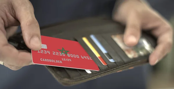 Homem puxa cartão de banco de plástico com bandeira de Marrocos fora de sua carteira, número de cartão fictício — Fotografia de Stock