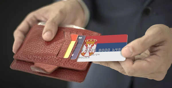 El hombre saca una tarjeta de banco de plástico con la bandera de Serbia de su billetera, número de tarjeta de ficción — Foto de Stock