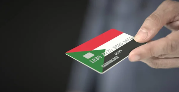 Ο άνθρωπος προσφέρει πλαστική τραπεζική κάρτα με τυπωμένη σημαία του Σουδάν, κοντινό πλάνο. Φανταστικοί αριθμοί — Φωτογραφία Αρχείου