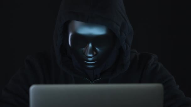 Desconocido hacker con ropa oscura y máscara negra funciona en su computadora portátil — Vídeos de Stock