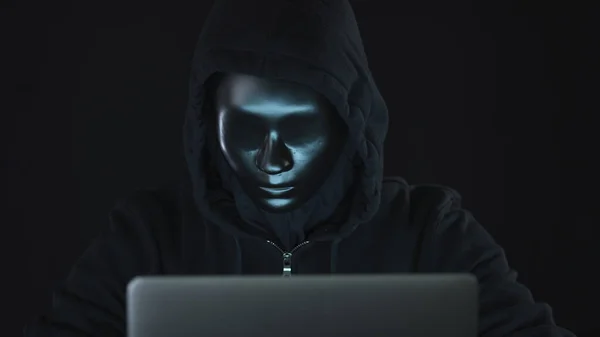 Hacker desconhecido ou robô vestindo roupas pretas e máscara usa o computador. botnet criminal ou hacking tiro conceitual — Fotografia de Stock