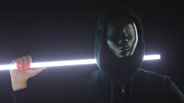 Ein anonymer Randalierer mit schwarzer Maske und Kapuze hält einen leuchtenden Lichtstab in der Hand. Protestkonzept — Stockvideo