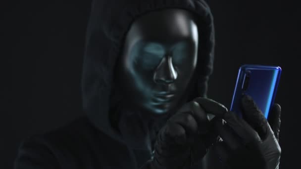 Hacker con máscara negra saca la pestaña WIRETAPPING de un teléfono inteligente. Concepto de hackeo — Vídeos de Stock