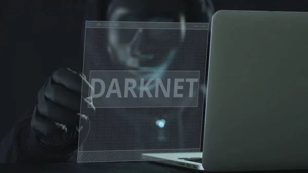 Hacker usando máscara preta puxa guia DARKNET de um laptop — Fotografia de Stock