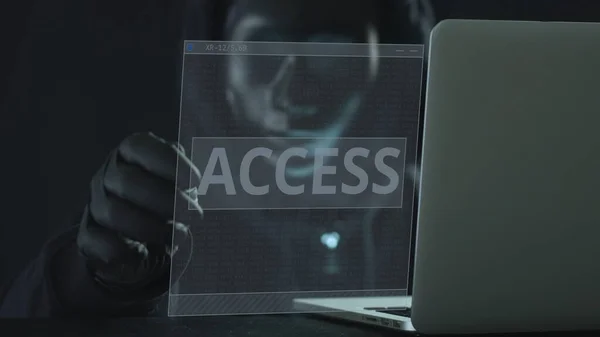 Hacker v černé masce vytáhne ACCESS kartu z notebooku — Stock fotografie