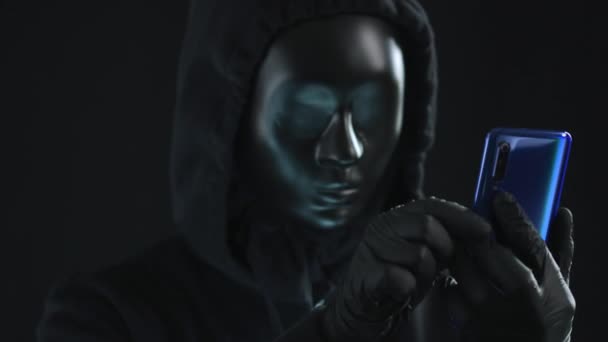 Hacker con máscara negra extrae la pestaña INFORMACIÓN de un teléfono inteligente. Concepto de hackeo — Vídeo de stock