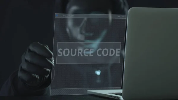 Hacker v černé masce vytáhne SOURCE CODE kartu z notebooku. Koncept hackování — Stock fotografie
