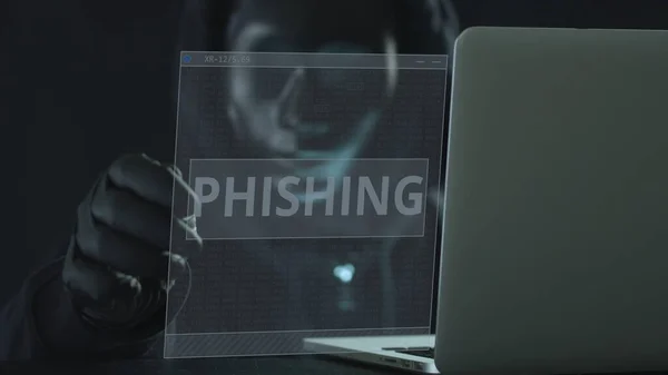 Hacker desconhecido usando máscara preta puxa guia PHISHING de um laptop. Conceito de hacking — Fotografia de Stock