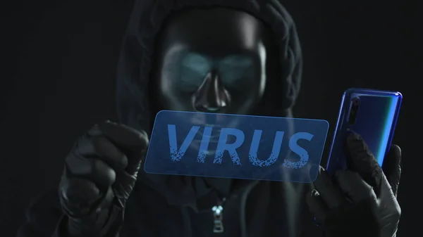 Haker w czarnej masce wyciąga kartę VIRUS ze smartfona. Koncepcja hakowania — Zdjęcie stockowe