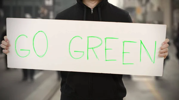 Aktivist in Schwarz hält ein Plakat mit GO GREEN Text in der Hand — Stockfoto