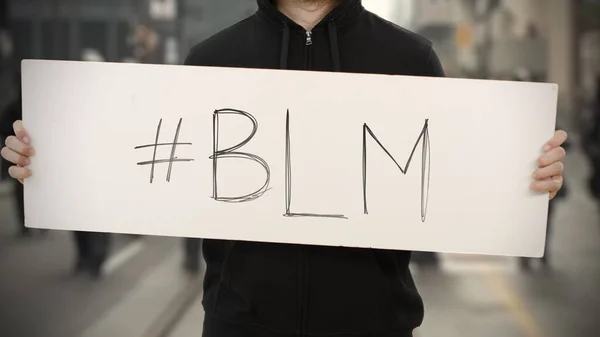 Activista vistiendo ropa oscura sostiene un cartel con BLM o etiqueta Black Lives Matter —  Fotos de Stock