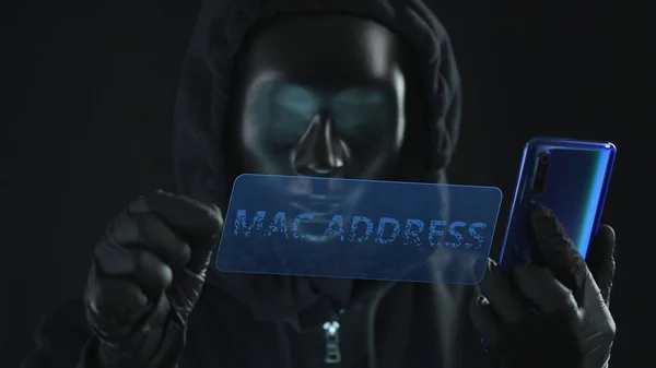 Hacker usando máscara preta puxa guia MAC ADDRESS de um smartphone. Conceito de hacking — Fotografia de Stock