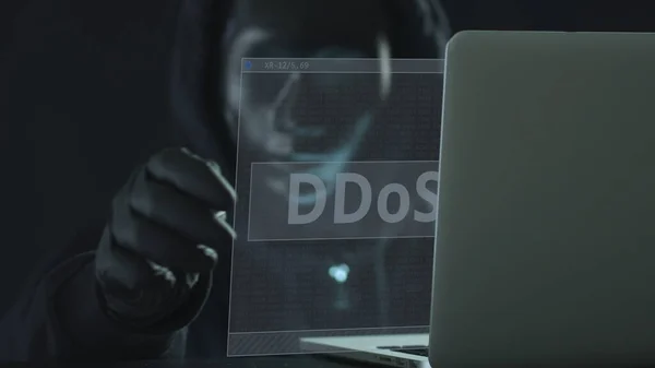Hacker v černé masce vytáhne DDoS kartu z notebooku — Stock fotografie