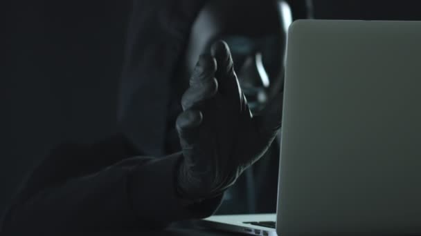 Hacker indossando maschera nera tira scheda DDoS da un computer portatile — Video Stock