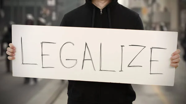 Ακτιβιστής φορώντας μαύρα κρατά μια πινακίδα με το κείμενο LEGALIZE — Φωτογραφία Αρχείου