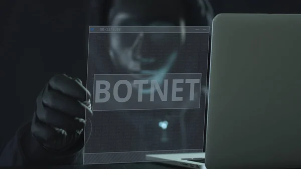 Un hacker vestido de negro saca BOTNET ficha de un ordenador portátil. Concepto de hackeo —  Fotos de Stock