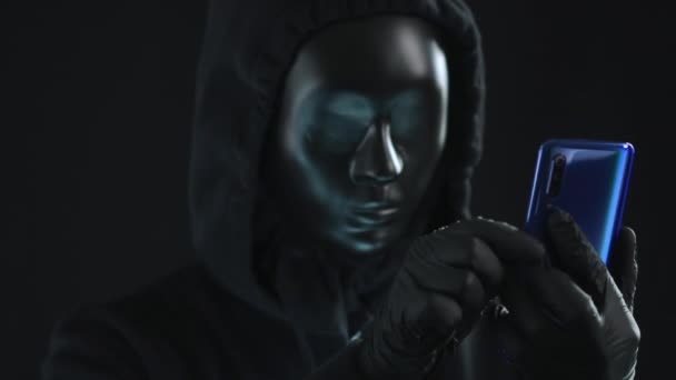 ブラックマスクを着用しているハッカーは、スマートフォンからデータベースタブを取得します。ハッキングの概念 — ストック動画