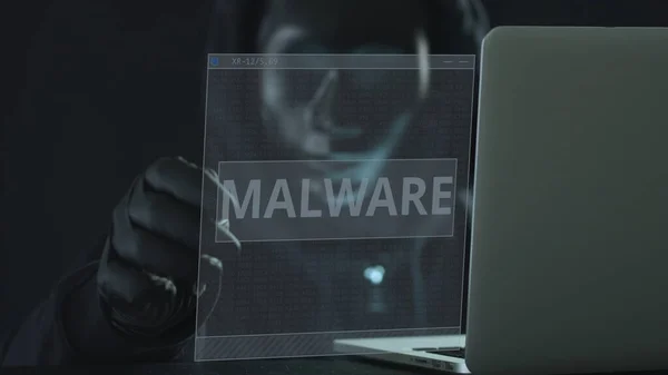 Hacker desconhecido usando máscara preta puxa guia MALWARE de um laptop. Conceito de hacking — Fotografia de Stock