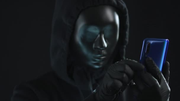 Hacker bär svart mask drar PERSONUPPGIFTER fliken från en smartphone. Hacka koncept — Stockvideo